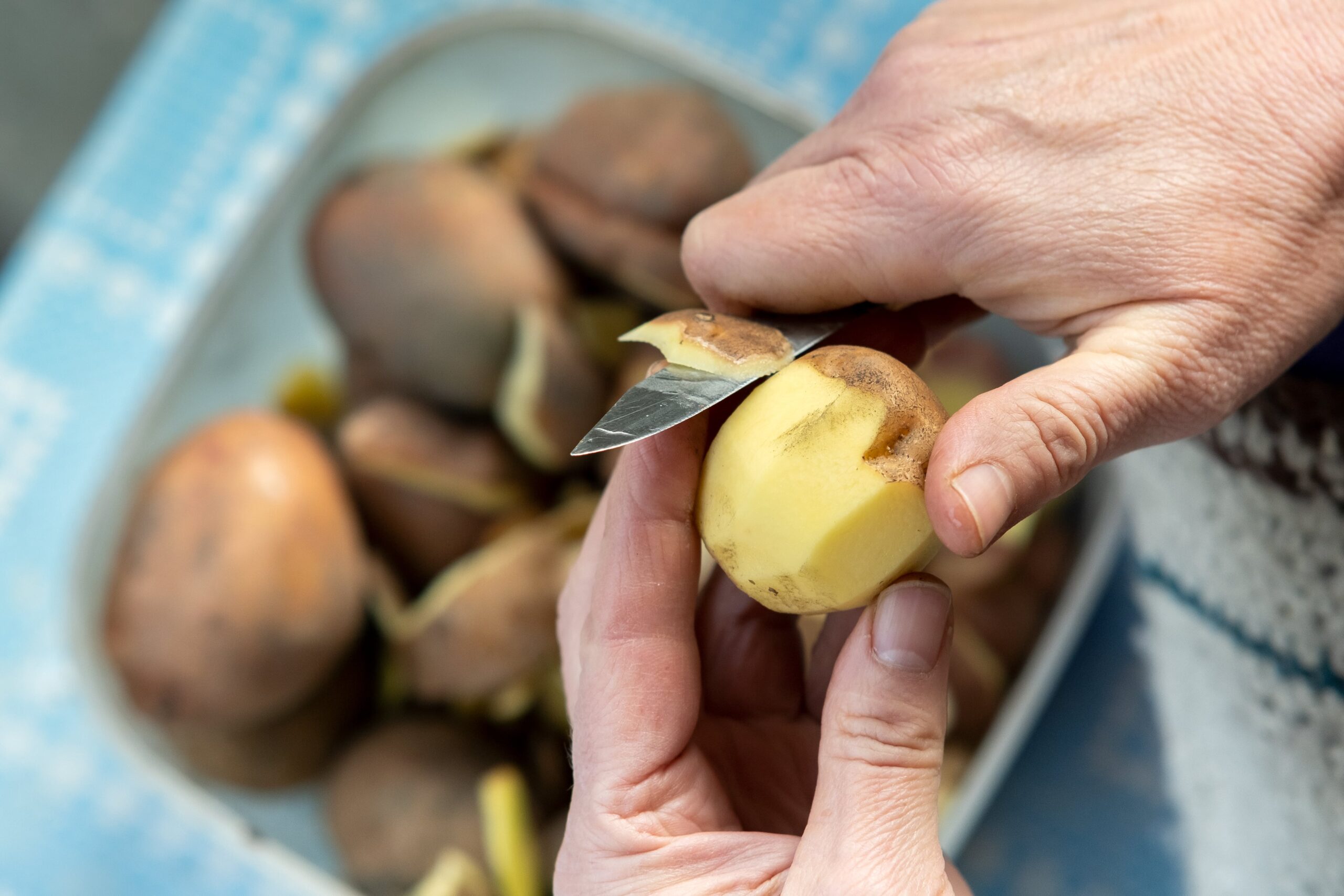 mani di donna che pelano patate con coltello